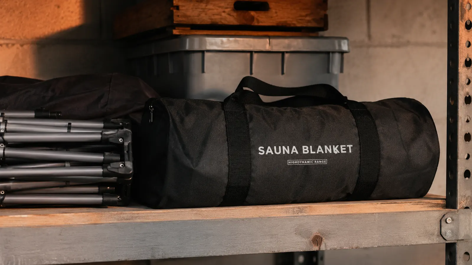 A rolled infrared sauna blanket sitting next to a folded pop-up sauna tent frame in a garage